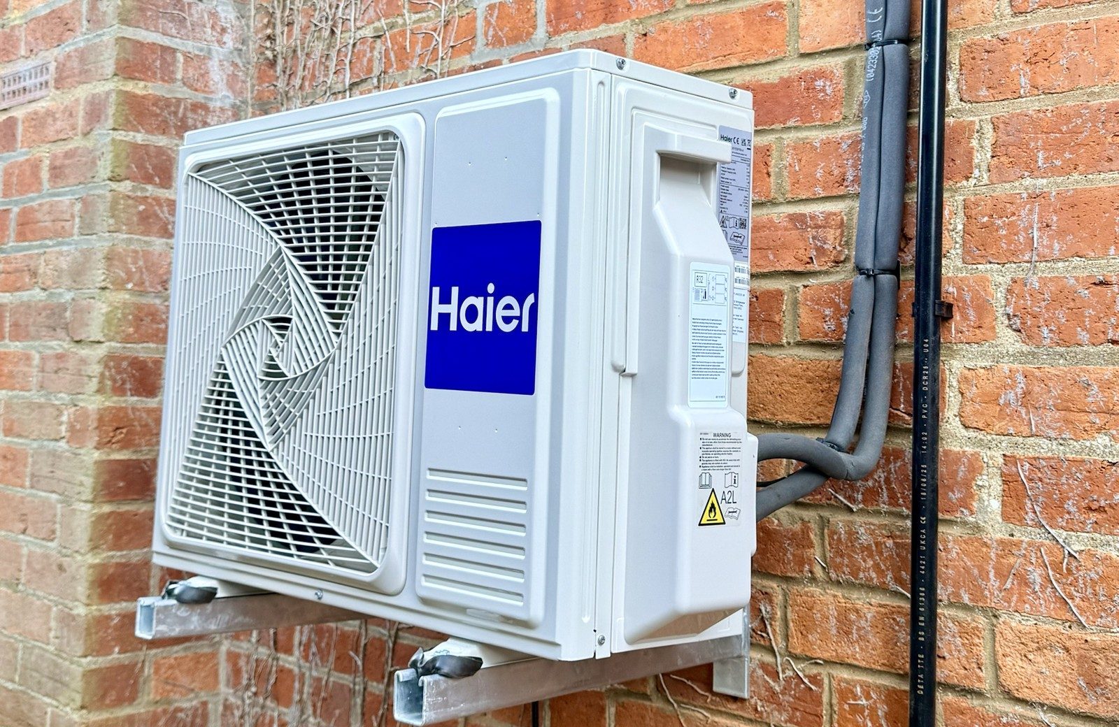 Haier outdoor unit on galvanised wall brackets with insulated pipework on a brick wall