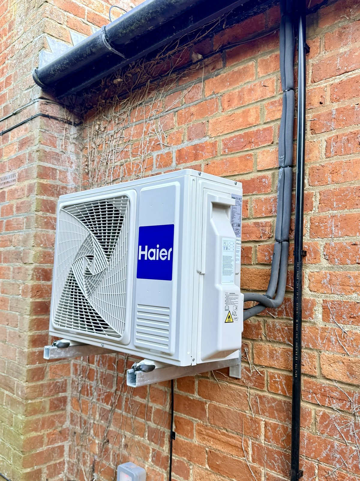 Haier outdoor heat pump unit on a wall bracket against a red brick wall