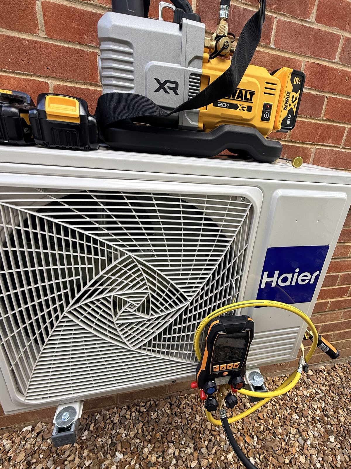 Haier outdoor unit on mounting feet with a vacuum pump and digital refrigeration gauges connected