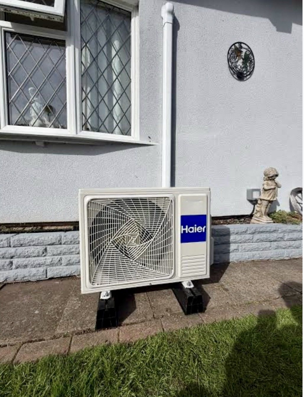 Haier outdoor heat pump unit on a ground stand beside a rendered bungalow in Buckingham