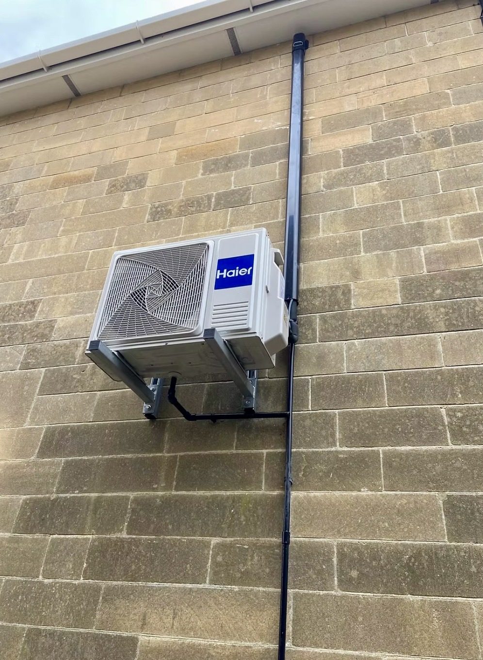 Haier outdoor air conditioning unit on a high wall bracket on a stone-effect brick house in Towcester