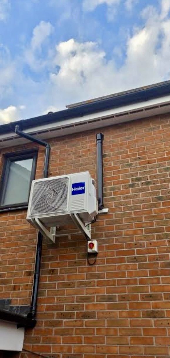 Haier outdoor heat pump unit on a wall bracket on a red brick house in Bicester, with an isolator switch below