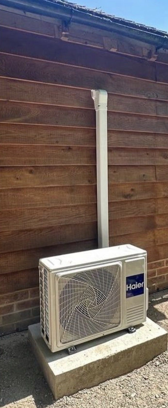 Haier outdoor heat pump unit on a concrete plinth beside a timber-clad garden building in Aylesbury